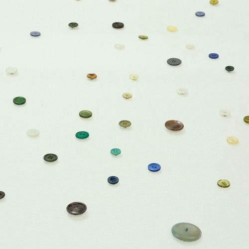 Talrijke kleine, kleurrijke knoopjes van verschillende groottes en tinten zijn verspreid over een lichtgekleurd, gestructureerd oppervlak.