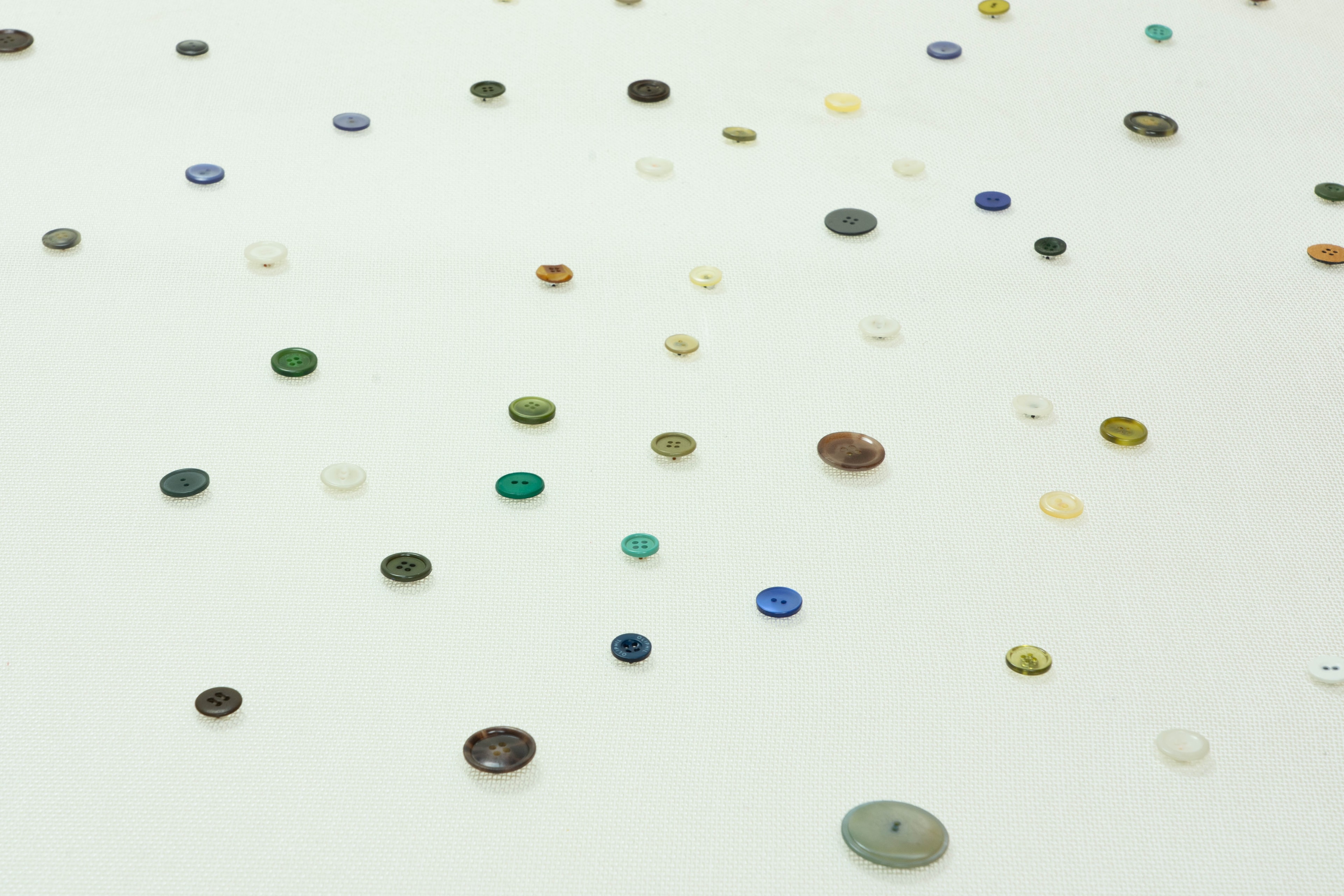 Talrijke kleine, kleurrijke knoopjes van verschillende groottes en tinten zijn verspreid over een lichtgekleurd, gestructureerd oppervlak.
