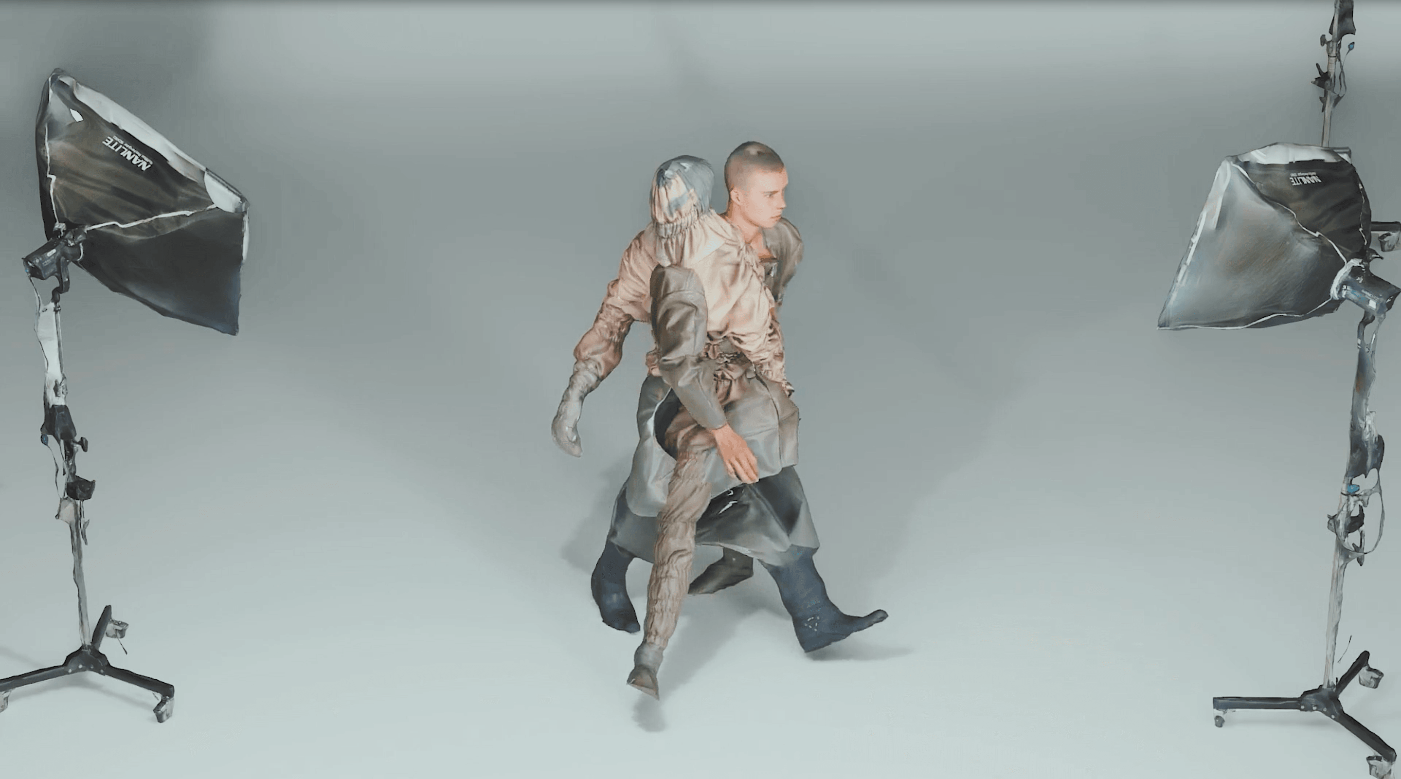 Een jonge man en een sculpturaal figuur in gelaagde kleding lopen een studio binnen met twee Nanlite softboxen.