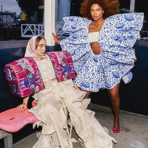 Twee modellen in high fashion: één met roze hoofddoek, rood jasje, kanten broek; de ander met afro, blauw-witte theepotjurk.