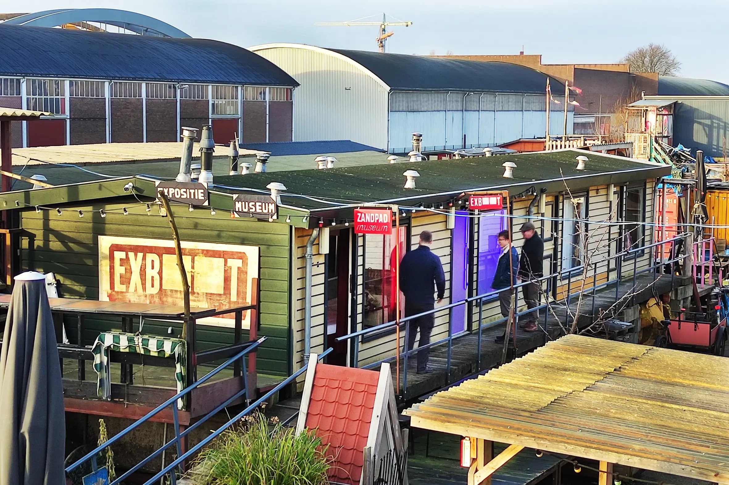 EXboot in de namiddagzon; bezoekers kijken door het raam naar binnen
